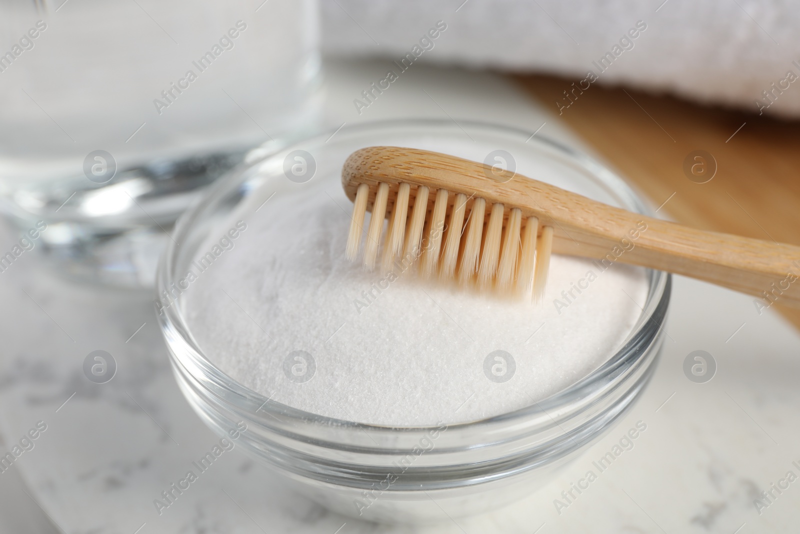 Photo of Bamboo toothbrush and glass bowl of baking soda on white marble table, closeup