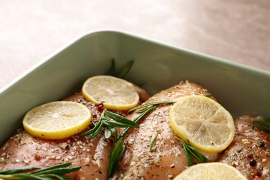 Photo of Chicken breasts with lemon and rosemary on grey table, closeup