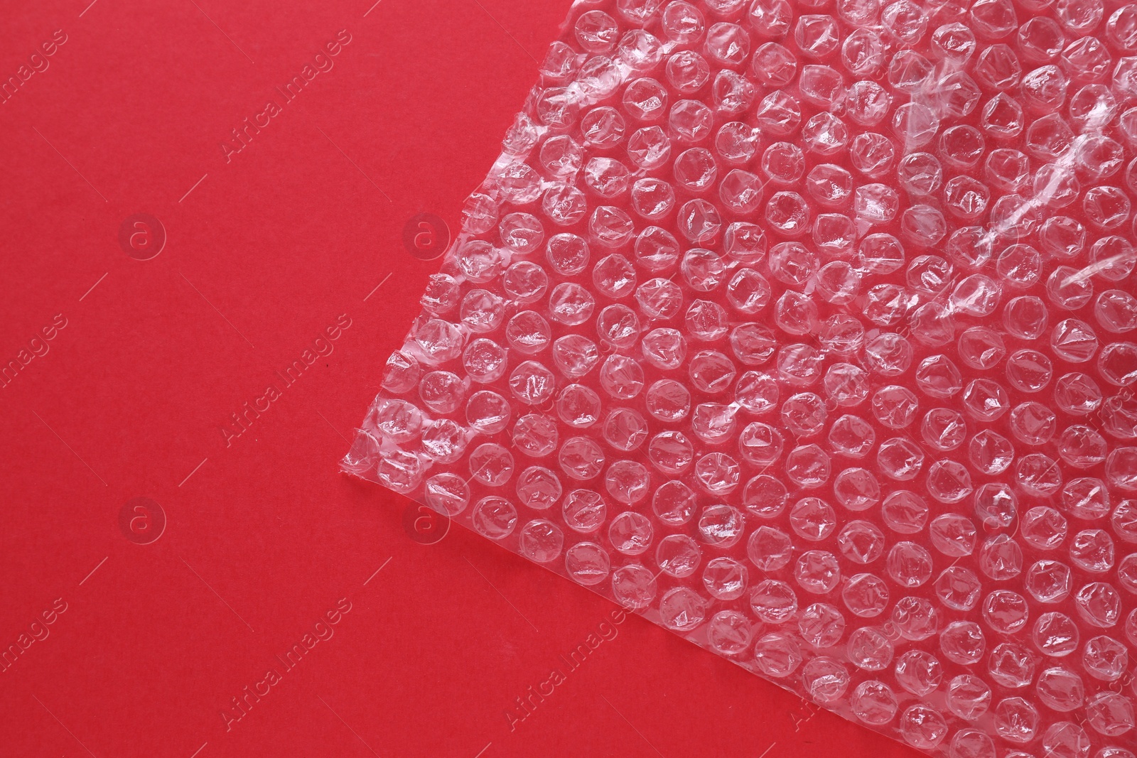 Photo of Transparent bubble wrap on red background, top view. Space for text