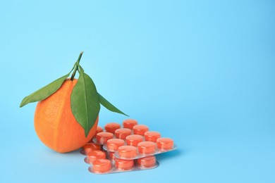 Photo of Fresh orange and blisters with cough drops on light blue background. Space for text