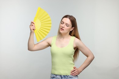 Photo of Beautiful woman waving yellow hand fan to cool herself on light grey background