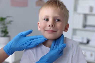 Endocrinologist examining boy's thyroid gland indoors, closeup