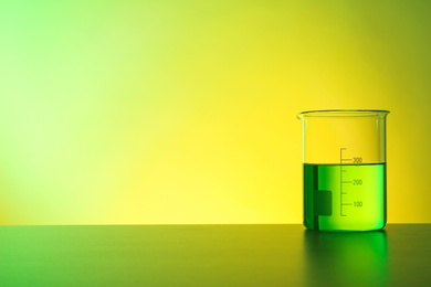 Beaker with liquid on table against color background. Chemistry laboratory glassware