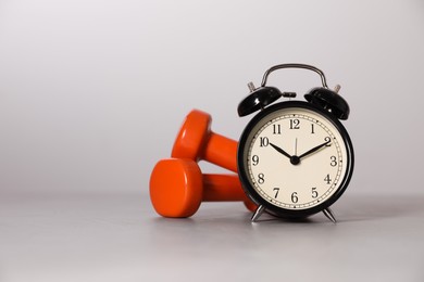 Photo of Alarm clock and dumbbells on grey background, space for text. Morning exercise