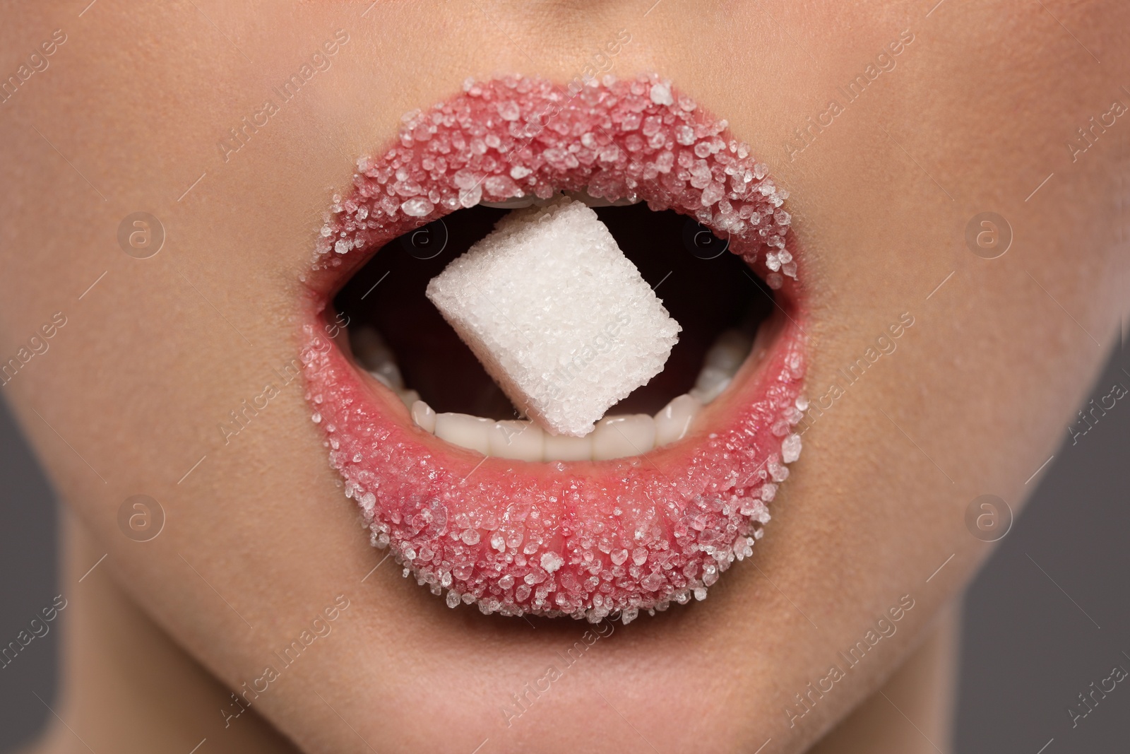 Photo of Woman with beautiful lips eating sugar cube on grey background, closeup