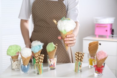 Woman holding waffle cone with cotton candy indoors, closeup