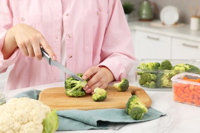 Photo of Woman cutting green broccoli near containers with fresh products at white marble table in kitchen, closeup