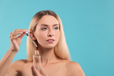 Photo of Beautiful woman with cosmetic serum in her hands on light blue background, space for text