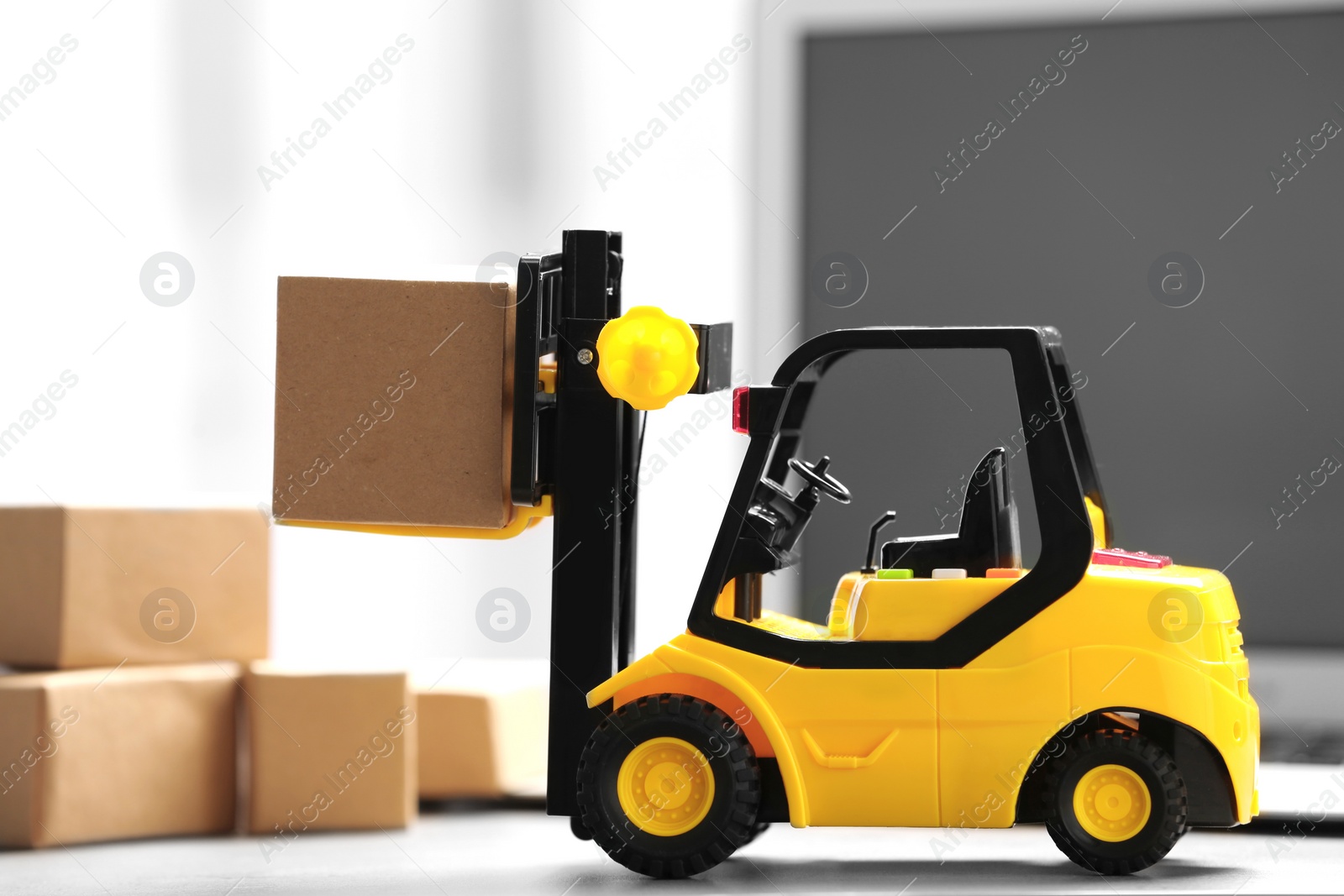 Photo of Toy forklift with box near laptop on table. Logistics and wholesale concept