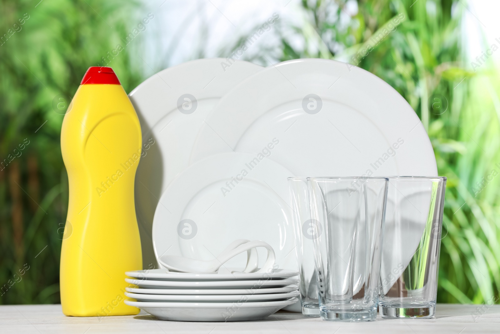 Photo of Set of clean dishware and detergent on white table against blurred background