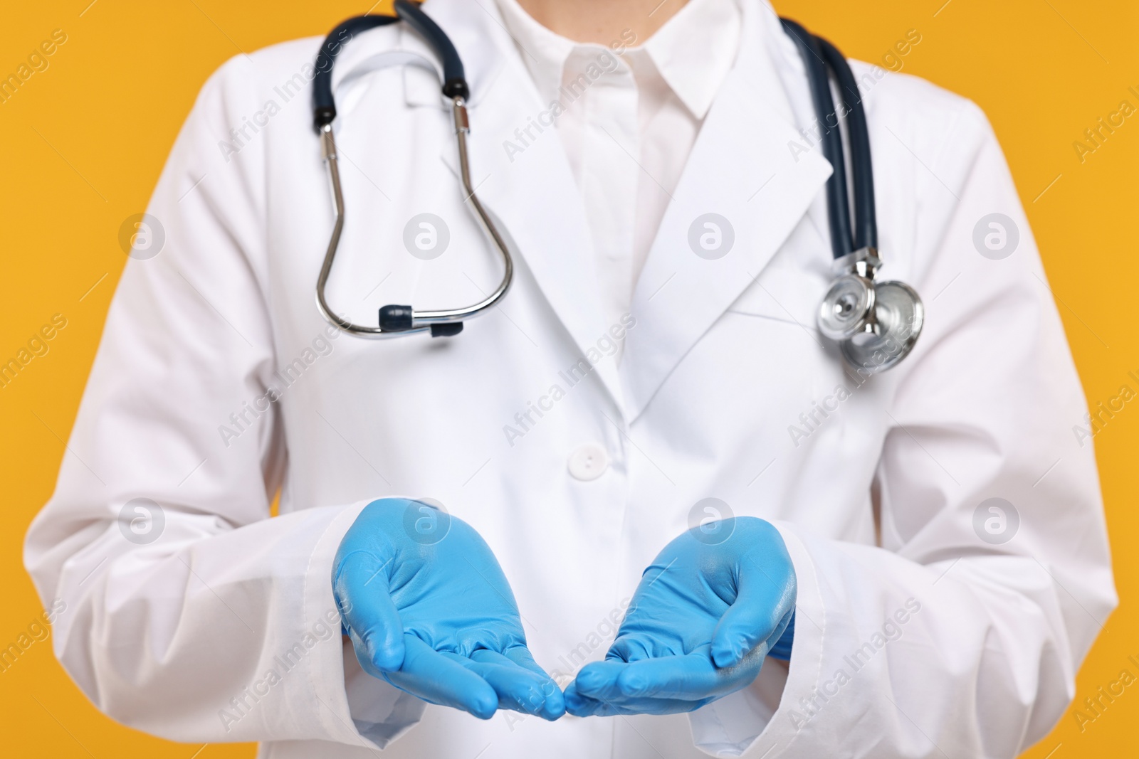 Photo of Doctor with stethoscope holding something on orange background, closeup