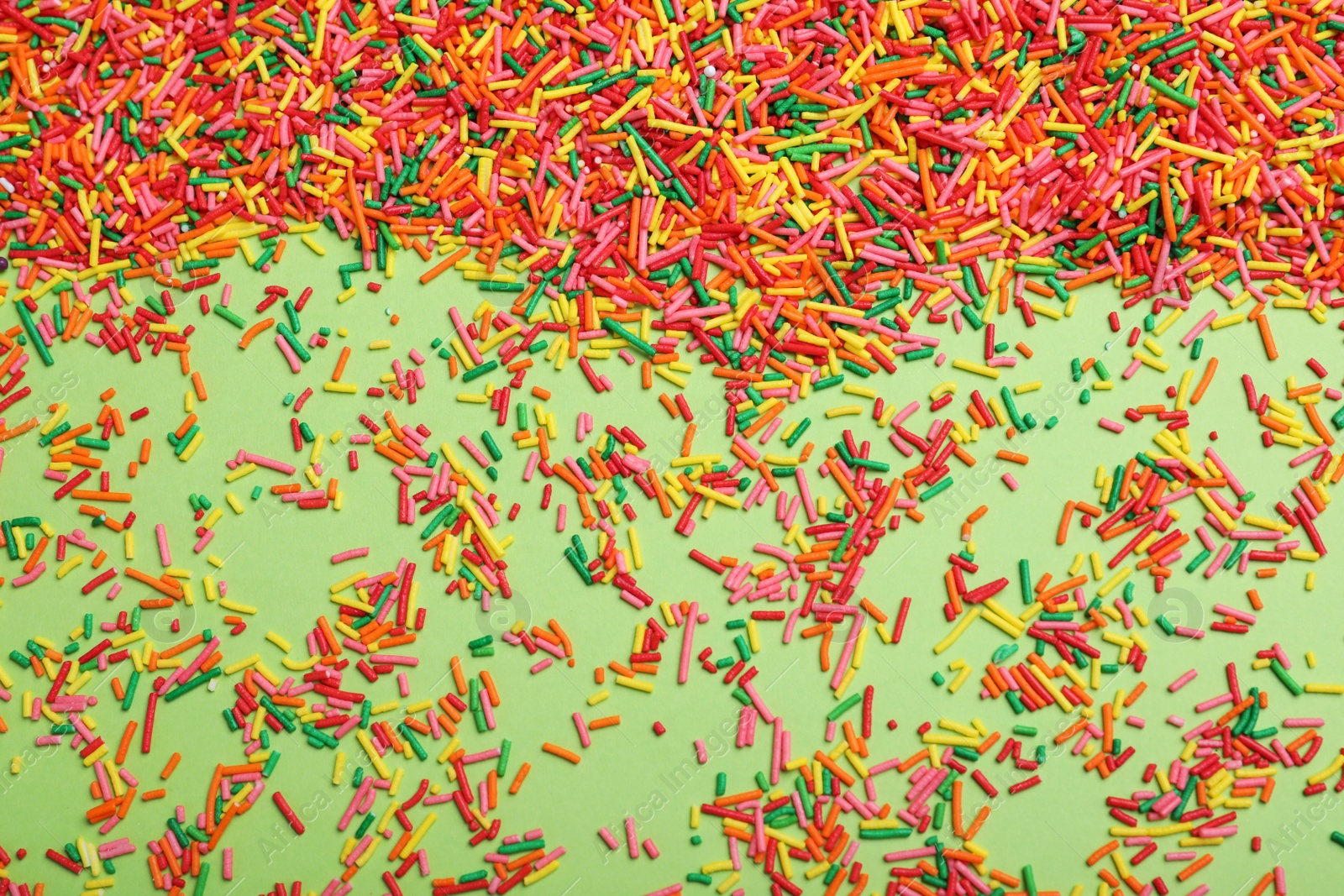 Photo of Colorful sprinkles on green background, flat lay. Confectionery decor