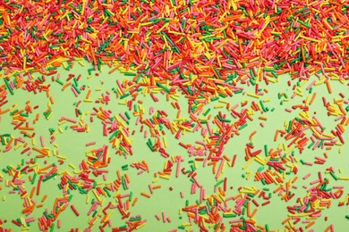 Photo of Colorful sprinkles on green background, flat lay. Confectionery decor