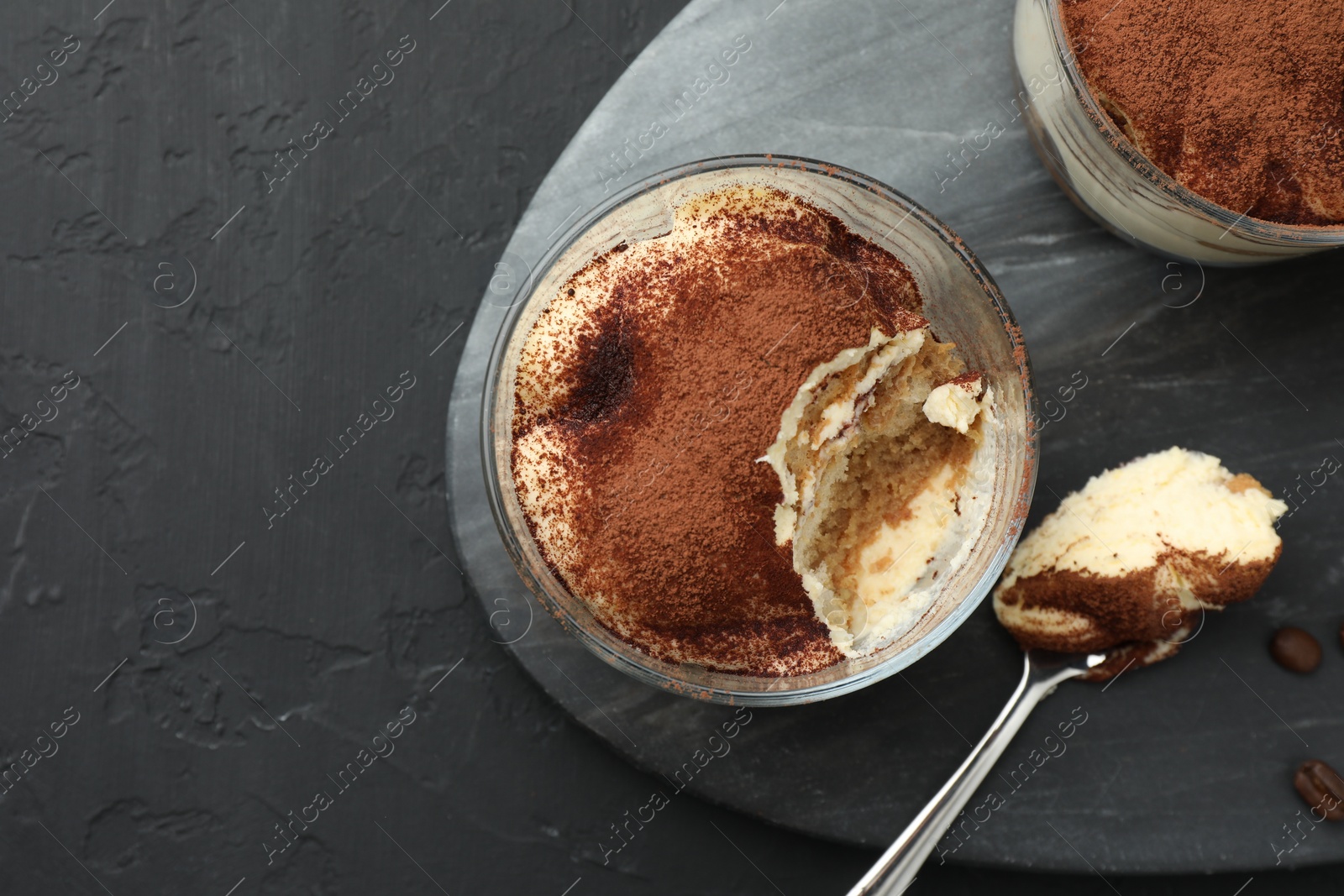 Photo of Delicious tiramisu in glasses and spoon on black table, top view. Space for text