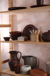 Set of different crafting tools and clay dishes on wooden rack in workshop