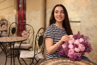 Photo of Beautiful woman with bouquet of spring flowers in outdoor cafe, space for text