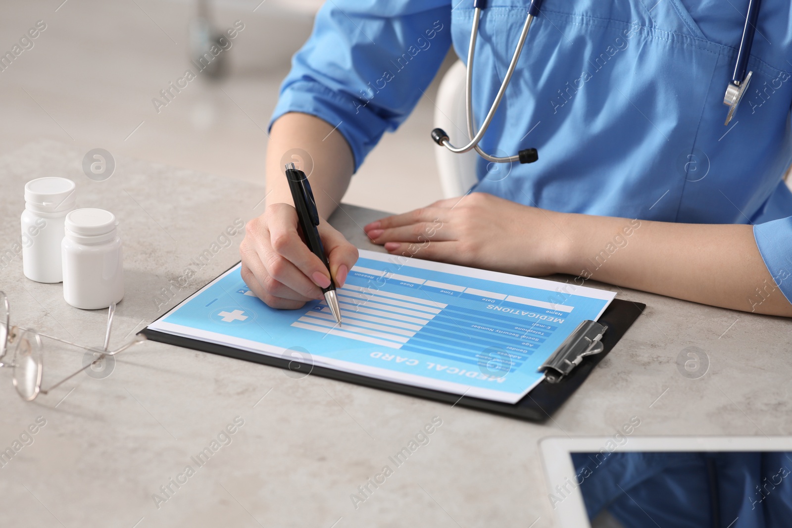 Photo of Doctor filling patient's medical card at table in clinic, closeup