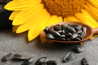 Photo of Spoon with sunflower seeds and flower on table, closeup