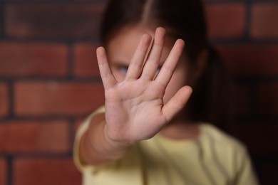 Photo of Child abuse. Little girl doing stop gesture near brick wall, selective focus
