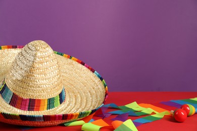 Photo of Mexican sombrero hat and maracas on red table, closeup. Space for text