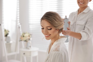 Photo of Professional stylist making wedding hairstyle for bride in salon