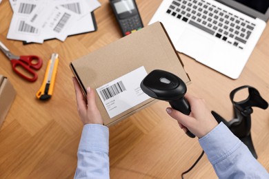 Photo of Parcel packing. Post office worker with scanner reading barcode at wooden table, top view