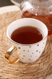 Photo of Aromatic tea in cup on wicker mat, closeup