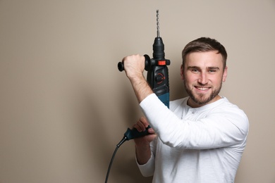 Young working man with rotary hammer on beige background, space for text