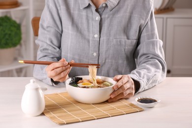 Photo of Woman eating delicious ramen with chopsticks at white table indoors, closeup. Noodle soup