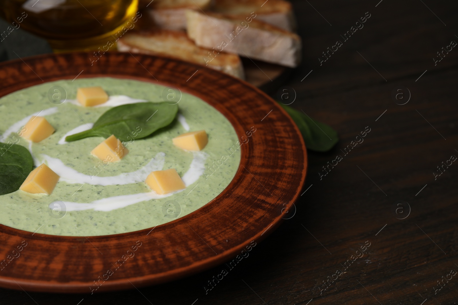 Photo of Delicious spinach cream soup with leaves and cheese in bowl on wooden table, closeup. Space for text