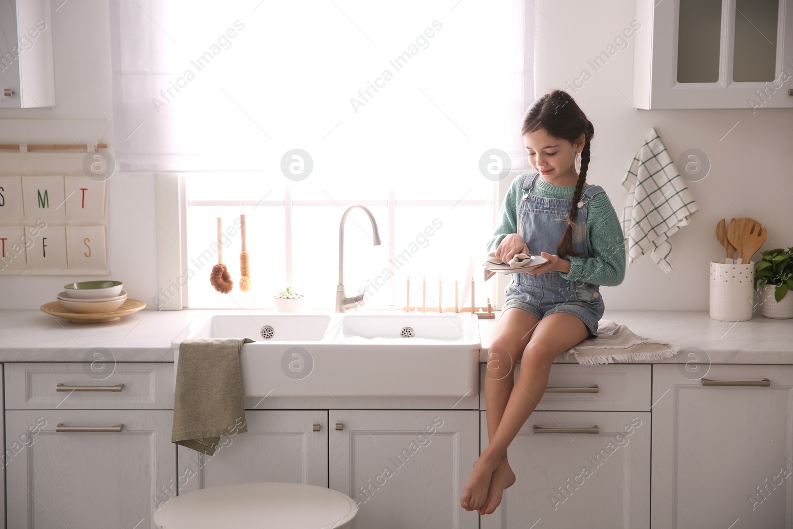 Photo of Little girl wiping dishes in kitchen at home