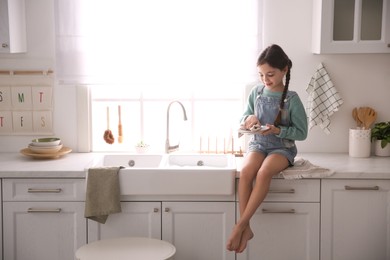 Photo of Little girl wiping dishes in kitchen at home