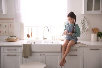 Little girl wiping dishes in kitchen at home