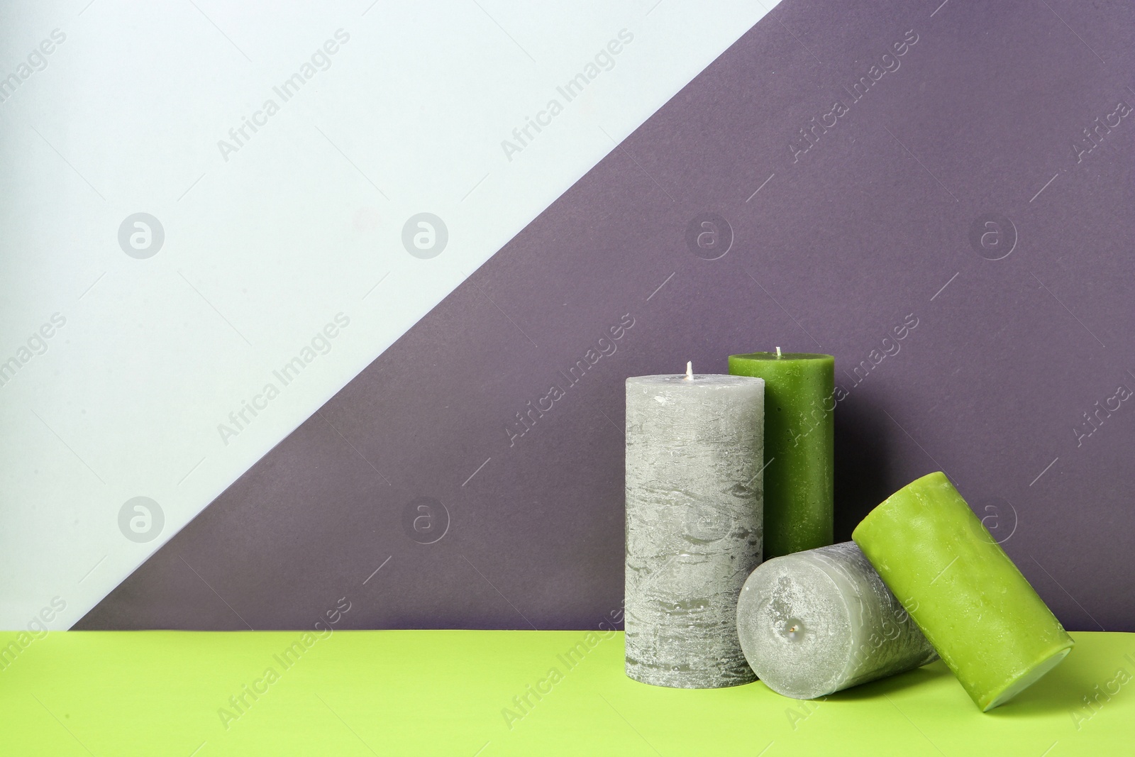 Photo of Different decorative wax candles on table against color background