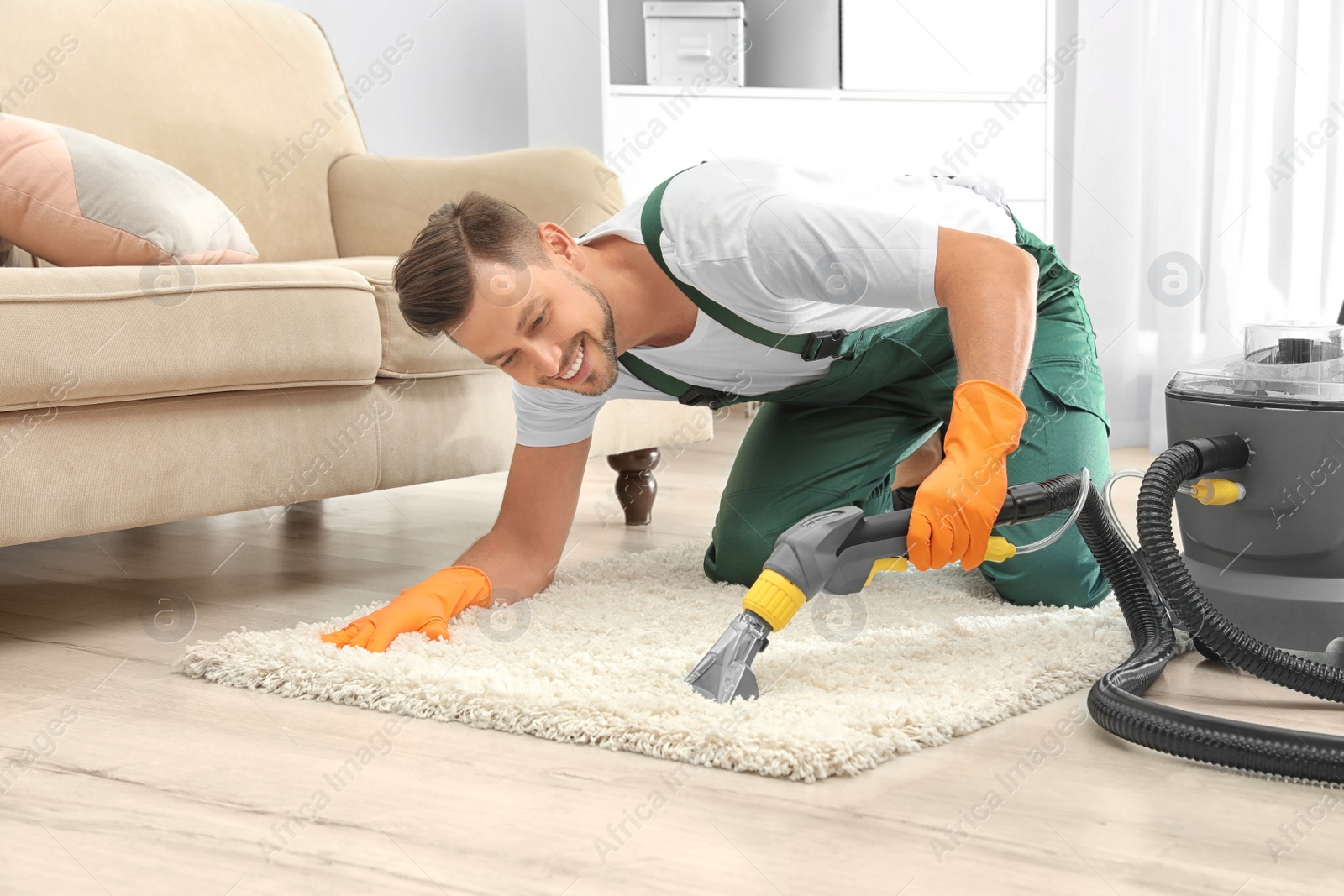 Photo of Male janitor removing dirt from rug with carpet cleaner in room