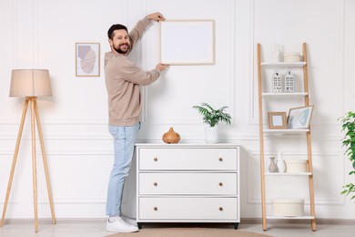 Man hanging picture frame on white wall at home