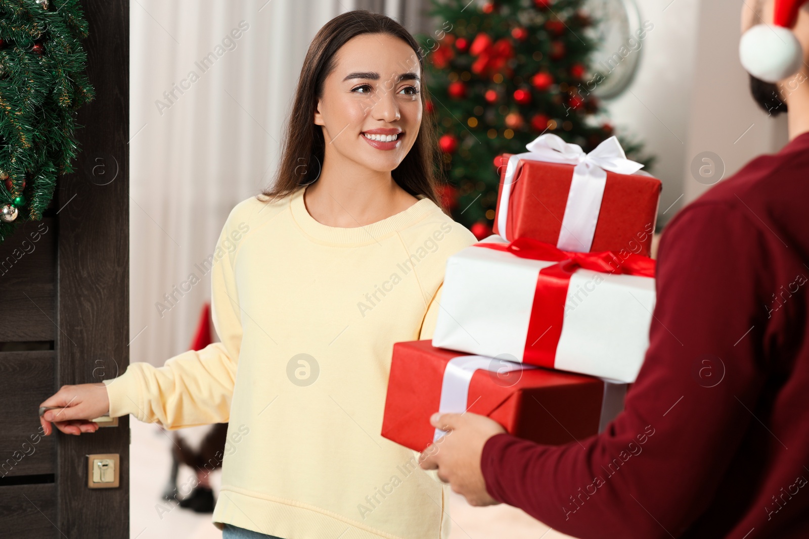 Photo of Courier giving young woman Christmas gift boxes indoors. Sending present by mail