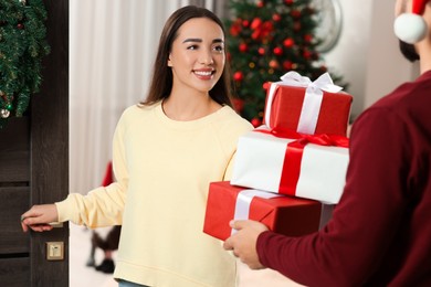 Courier giving young woman Christmas gift boxes indoors. Sending present by mail