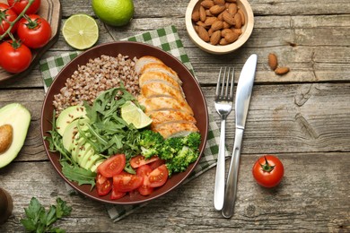 Photo of Healthy meal. Tasty products in bowl, ingredients and cutlery on wooden table, flat lay