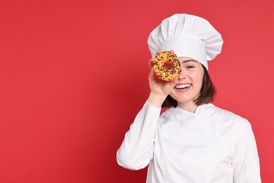 Photo of Happy confectioner with delicious donut on red background, space for text
