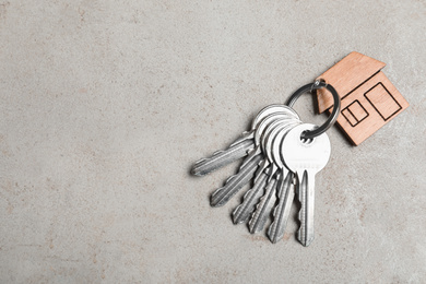 Keys with trinket in shape of house on grey stone background, top view and space for text. Real estate agent services