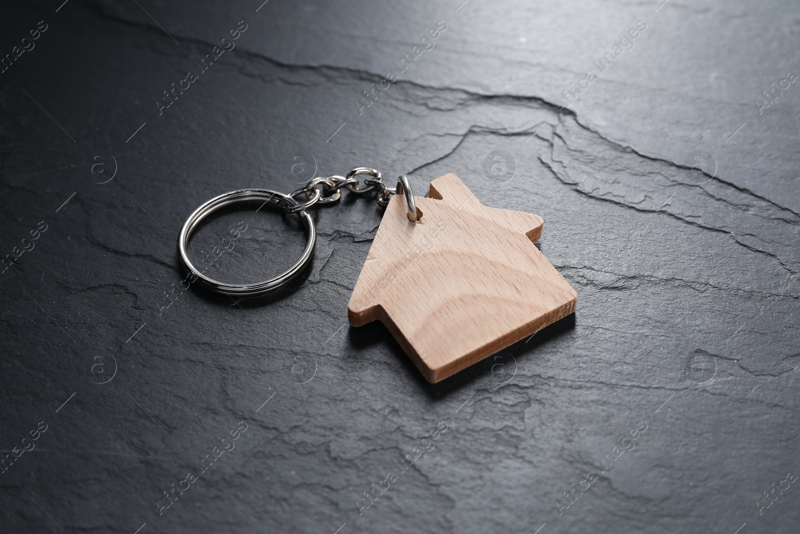 Photo of Wooden keychain in shape of house on dark textured table, closeup