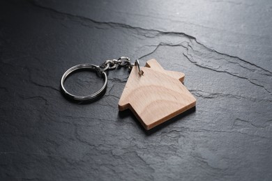 Photo of Wooden keychain in shape of house on dark textured table, closeup