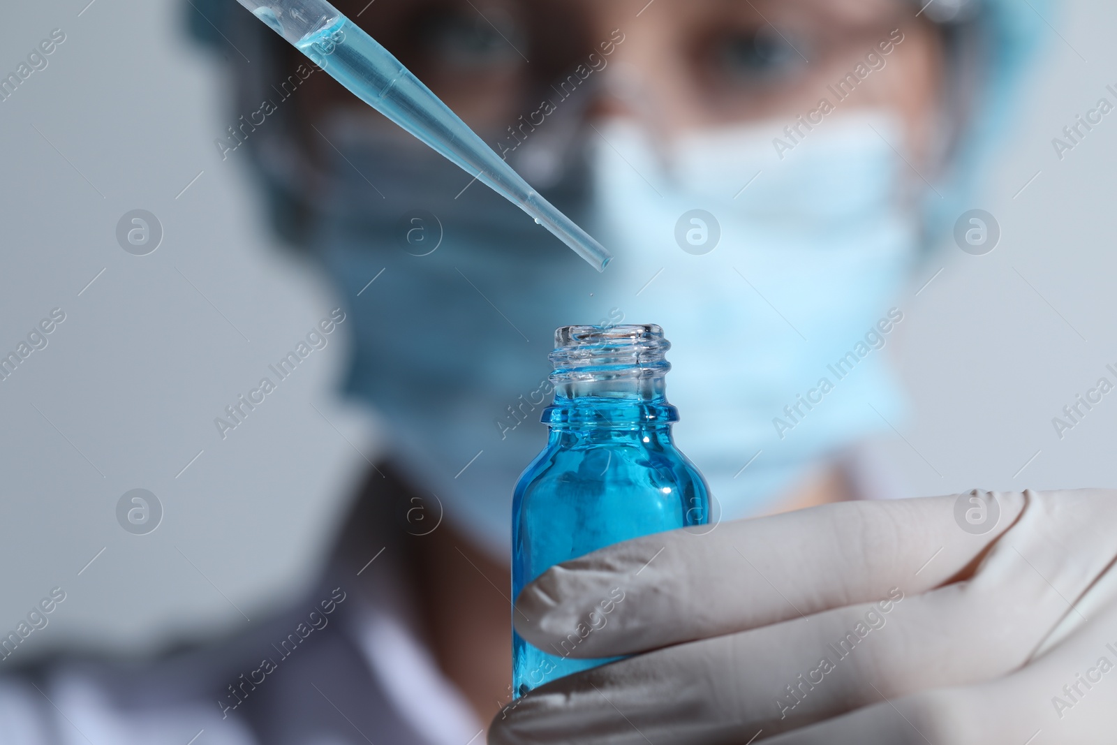 Photo of Scientist dripping liquid from pipette into glass bottle on light background, closeup