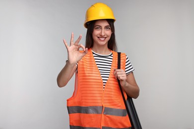 Architect in hard hat with tube showing ok gesture on light grey background