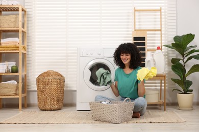 Happy woman with laundry near washing machine indoors