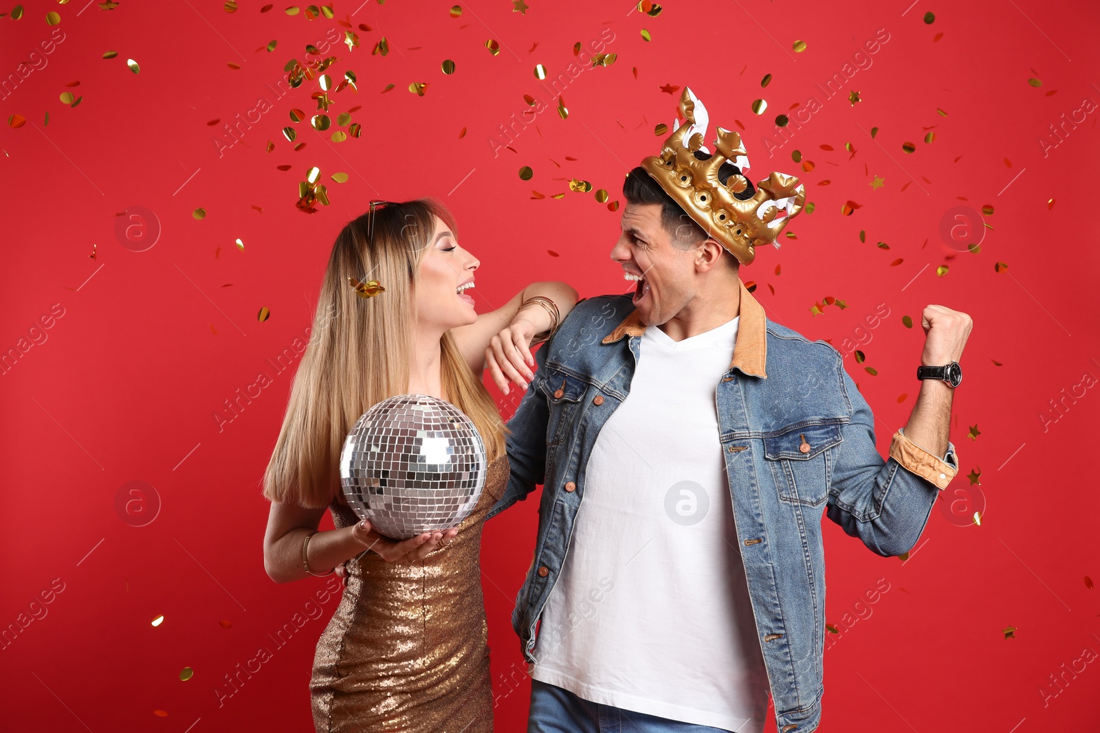 Photo of Happy couple with disco ball and confetti on red background