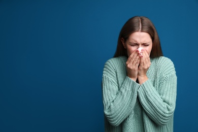 Image of Young woman sneezing on blue background, space for text. Cold symptoms