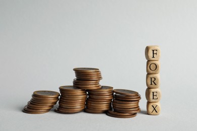 Photo of Word Forex made of wooden cubes with letters and stacked coins on light grey background
