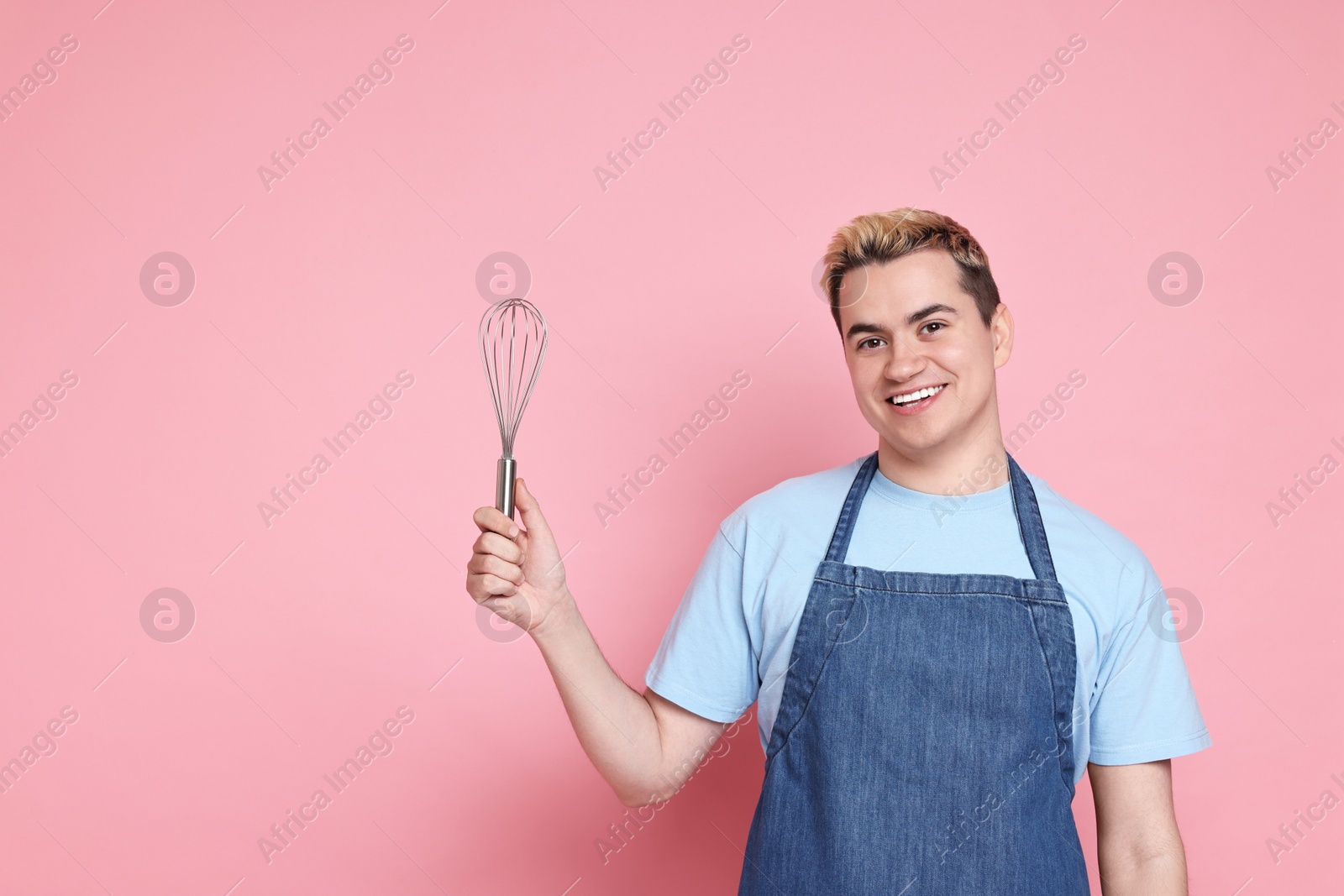 Photo of Portrait of happy confectioner holding whisk on pink background, space for text